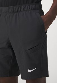 Pantalones cortos deportivos negros con cintura elástica, bolsillos laterales y una abertura en el dobladillo. Presentan un logo de Nike en blanco en la parte inferior de la pierna.