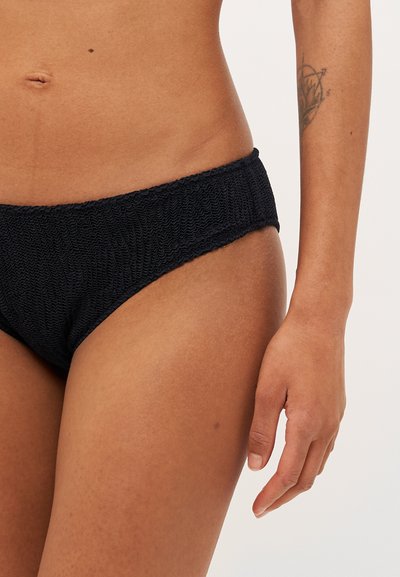 Melnas bikini apakšda, kas izgatavota no teksturēta auduma ar savilktu jostasvietu, ar vienkāršu dizainu un smalkiem šuvumu elementiem.