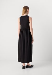 Svart ermeløs maxikjole med tettsittende bodice og rynket midje, laget av mykt stoff. Kombinert med svarte flate sko.
