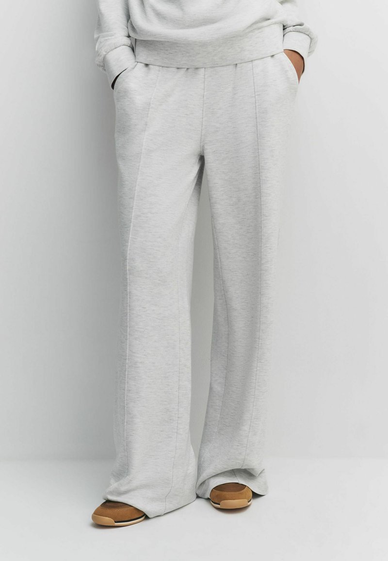 Light grey wide-leg sweatpants in soft fabric with side pockets and subtle stitching details, paired with brown and tan sneakers.