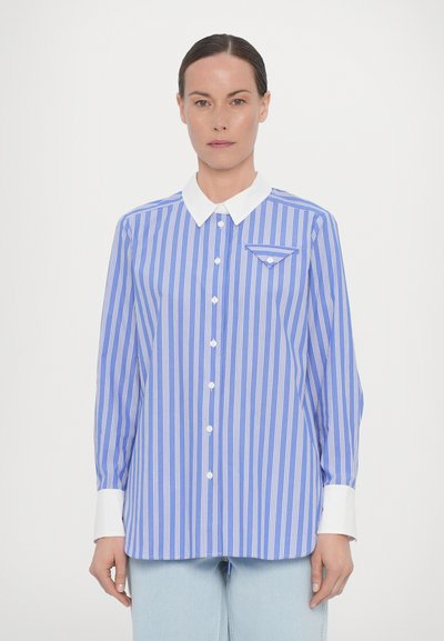 Lichtblauw shirt met witte strepen, witte kraag, lange mouwen en een borstzak. De stof heeft een soepele textuur met knoopsluiting.
