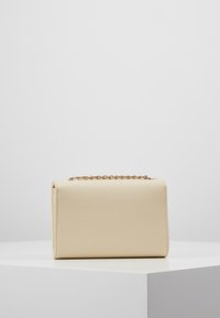 Beige textured handbag with a structured shape, featuring a gold chain strap and a smooth interior. Minimalist design with no visible hardware.