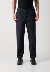 Marineblauwe katoenen broek met een rechte pasvorm, voorzien van een knoopsluiting, zijzakken en een soepele textuur. Gekoombineerd met zwarte schoenen.