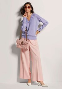 Hellblauer V-Ausschnitt-Pullover, pinke weit geschnittene Hose, weiße Slingback-Absätze und eine strukturierte pinke Handtasche mit goldenen Akzenten.