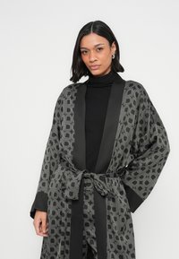 Mustast kimonolikust hommikumantel geomeetrilise mustriga, kontrastse satiinist äärisega, pikkade varrukatega ja vööga. Pehme kangas, sileda tekstuuriga.