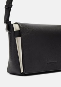 Czarna skórzana torebka na ramię o teksturowanym wykończeniu, z klapą, kremowym wnętrzem i wytłoczonym logo marki.