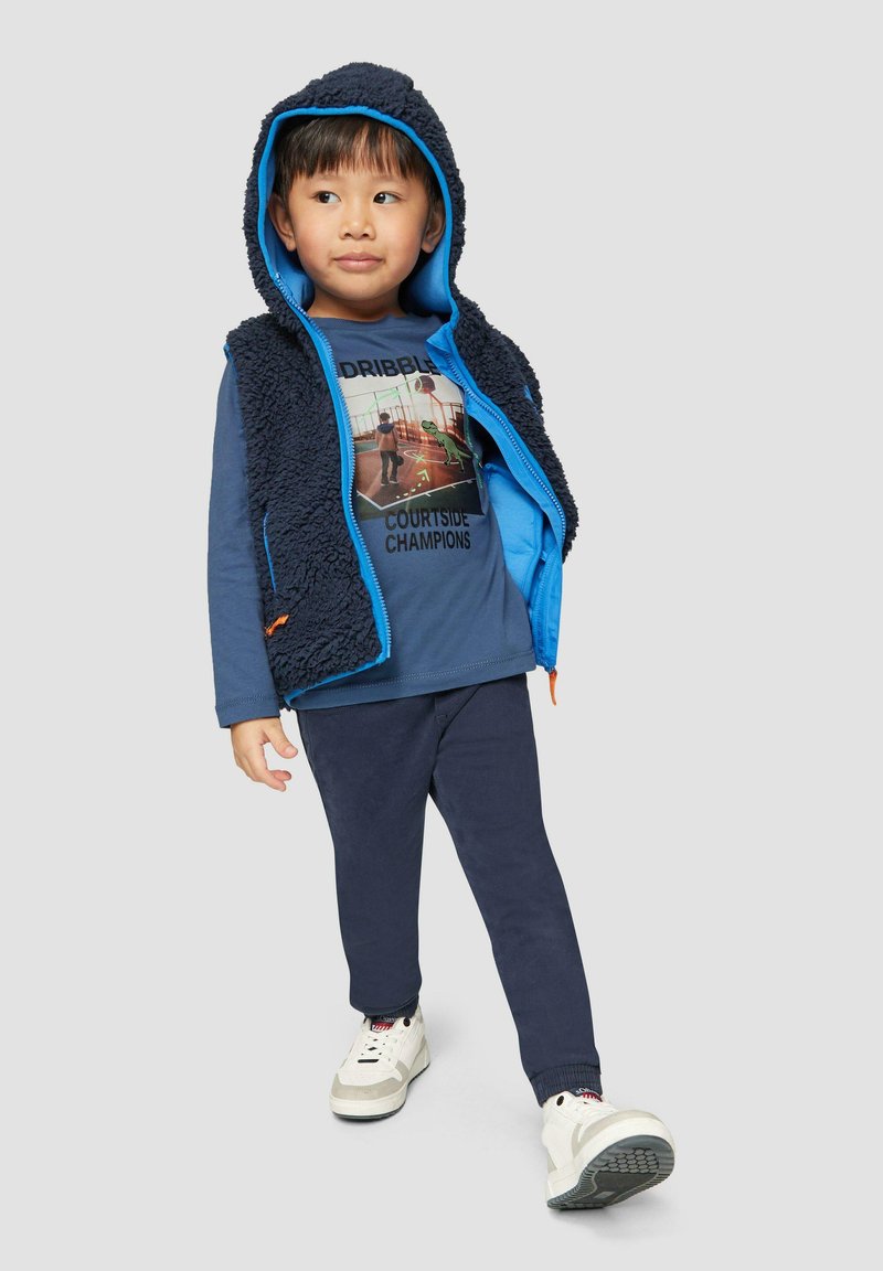 Blauer Fleece-Weste mit Kapuze und kontrastierender Innenausstattung, kombiniert mit einem navyfarbenen Langarmshirt mit grafischem Print und passenden Hosen.