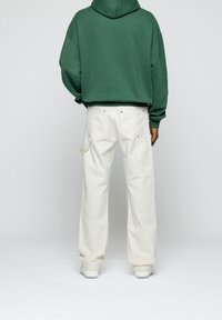 Sudadera verde con capucha, de corte relajado, con un bolsillo tipo canguro; combinada con pantalones blancos de corte holgado que presentan bolsillos laterales y detalles de costura.