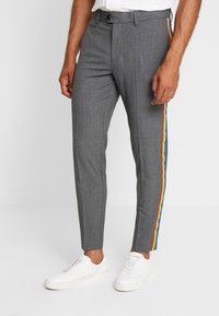 Šedé slim-fit kalhoty s duhovým pruhem na boku, mají hladkou texturu, pás s opaskem a jsou spárovány s bílými teniskami.