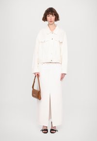 Bela jeans jakna s srebrnimi gumbi, dolga bela krila s sprednjim razporkom, rjava torbica in črne sandale z dekorativnimi mašnjami.