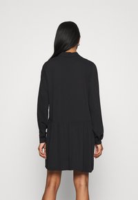 Abito lungo nero con maniche a sbuffo, colletto, polsini abbottonati e una gonna svasata a strati. Tessuto liscio, design minimalista e senza motivi visibili.