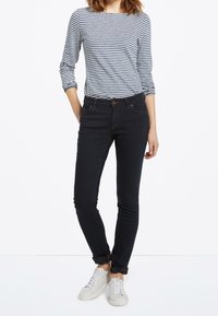Jeans skiny de mezclilla azul oscuro con una textura suave y puños enrollados, combinados con una camiseta de manga larga a rayas azul marino y blanca y zapatillas blancas.