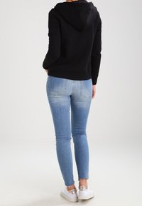 Svart hoodie med dragsko i huvan, kombinerad med ljusblå tajta jeans. Vita sneakers med metalliska detaljer. Bakre vy av outfiten.