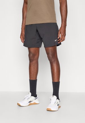 Zwarte sportshorts van lichtgewicht stof, gecombineerd met witte sneakers met zwarte accenten en donkergrijze geribde sokken.