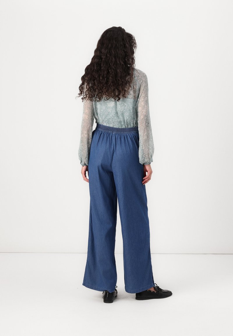 Blusa trasparente a fantasia blu chiaro con maniche lunghe abbinata a pantaloni in denim scuri a vestibilità comoda e scarpe nere flat.