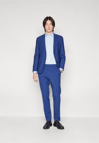 Herenblauw pak met een getailleerd jasje met notch-lapel en slim-fit broek, gecombineerd met een lichtblauw overhemd met knopen en zwarte schoenen.