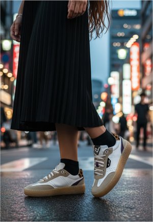 Weiße Sneakers mit beigen Akzenten, strukturierten Gummisohlen und lila Details, kombiniert mit schwarzen Socken und einem gefalteten schwarzen Rock.