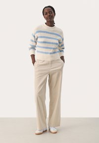 Pull léger rayé en crème et bleu, associé à un pantalon en corduroy beige à jambes larges. Chaussures incluant des baskets grises et blanches.