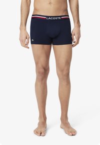 Boxer-briefs bleu marine avec une coupe ajustée, arborant une ceinture contrastante avec des rayures rouges et blanches ainsi qu'un petit logo vert sur la jambe.