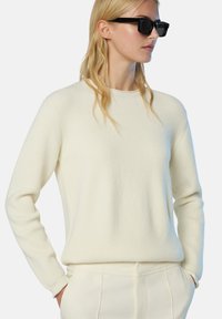 Maglione a coste di crema chiara con colletto rotondo, maniche lunghe e discrete finiture testurizzate, abbinato a pantaloni crema.