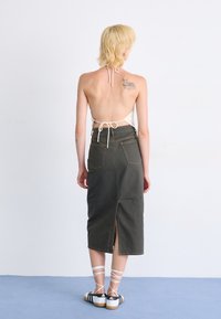 Halter top na chrbte z krémovej čipky, v kombinácii s tmavozelenou džínsovou sukňou s rozparkom na chrbte. Doplnky s bielymi čipkovanými topánkami.