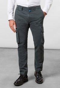 Šedé cargo kalhoty slim fit s dvěma bočními kapsami, měkkou texturou a modrým akcentem na pasu. Nosené s černými botami.