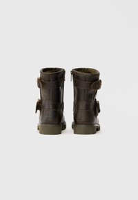 Botas de tornozelo em couro castanho com fecho de zíper, duas correias ajustáveis e detalhes texturizados. Solas de borracha grossa com um padrão de cravos.