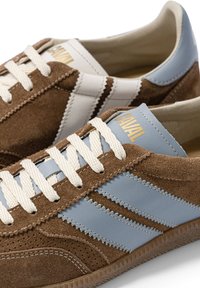 Paire de baskets en daim marron avec des rayures en cuir bleu clair et des lacets blancs, avec un logo doré "CAVAL" sur les languettes.