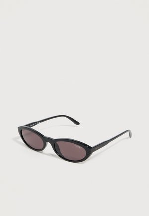 Gafas de sol negras de ojo de gato con lentes oscuras y la marca "Vogue" en la lente y las patillas, sobre un fondo blanco.