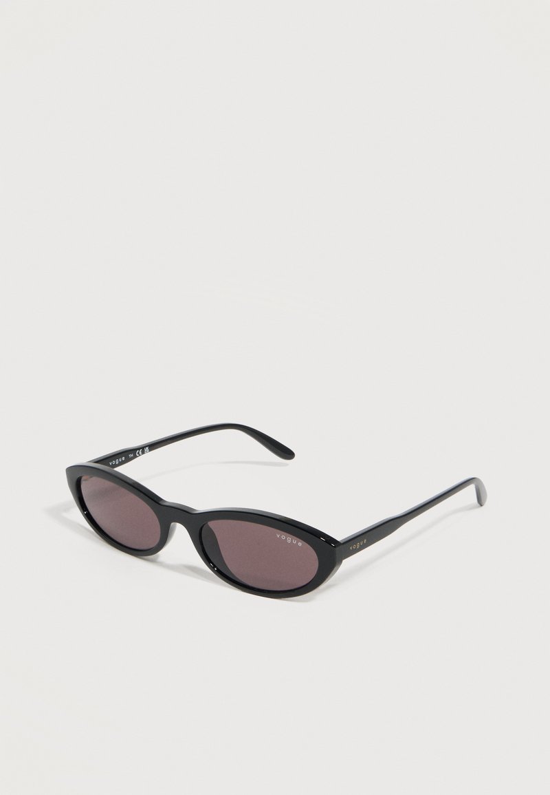 Γυαλιά ηλίου μαύρα σε στυλ cat-eye με σκοτεινούς φακούς και την επωνυμία «Vogue» στον φακό και στα πλαϊνά, με λευκό φόντο.