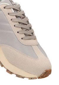 Zapatilla beige con una combinación de cuero liso y ante texturizado. Cuenta con seis agujetas redondeadas, puntera reforzada y una suela de goma con motas.
