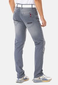 Helle, graue Denim-Hose mit slim fit, kontrastierenden Akzenten, mehreren Taschen und einem markierten Logo auf der Rückseite. Mit einem weißen Bund abgeschlossen.