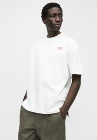 Λευκό βαμβακερό t-shirt με στρογγυλή λαιμόκοψη, κοντά μανίκια και μικρό ροζ λογότυπο στο αριστερό στήθος. Συνδυάζεται με παντελόνι σε ελιά απόχρωση.