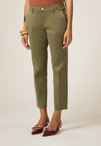 Chinos verde oliva con una vestibilità dritta, dotati di una tasca frontale e un accento decorativo di catena sulla cintura. Indossati con tacchi color bordeaux.