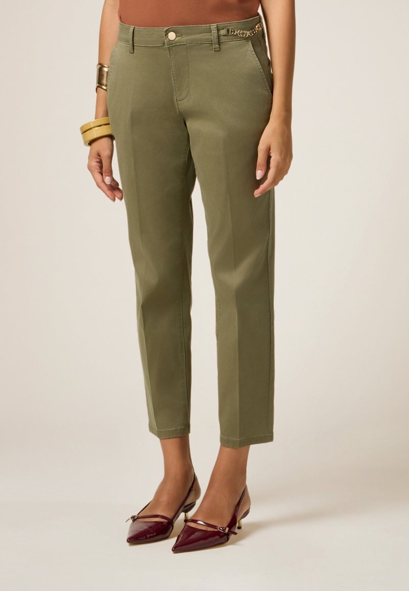 Chinos verde oliva con una vestibilità dritta, dotati di una tasca frontale e un accento decorativo di catena sulla cintura. Indossati con tacchi color bordeaux.