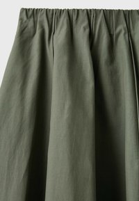 Tissu vert avec une ceinture élastique froncée et des plis subtils, montrant la texture et le drapé du matériau.