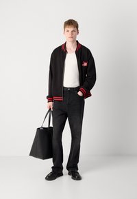 Black bomber jacket with red striped cuffs, white tank top, black jeans, and black tote bag. Black shoes complete the outfit.