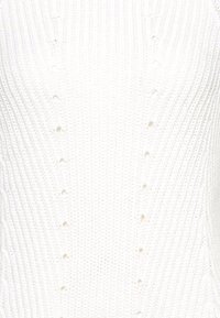 Witte gebreide trui met een textuurpatroon met verticale ribbels en kleine knoopsgaten in het midden voor sluiting of decoratie.