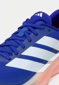 Μπλε αθλητικά παπούτσια από δίχτυ και συνθετικά υλικά με τρεις λευκές ρίγες, μπλε κορδόνια και υφή στη σόλα με ανοιχτό πορτοκαλί λεπτομέρεια.