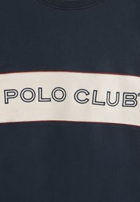 Felpa navy con una fascia orizzontale cream con il testo "POLO CLUB" ricamato in navy. Rifinita con un bordo rosso lungo la fascia.