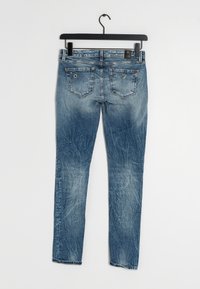 Jeans ajustados de color azul hechos de denim, con un acabado desgastado, dos bolsillos traseros con costuras decorativas y un lazo para colgar.