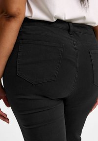 Mustat farkut, joissa on tiukka siluetti, perinteiset takataskut ja sileä, hieman joustava kangas.