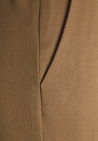 Brunt tyg med en slät yta och diagonala sömdetaljer. Materialet verkar vävt och har en något glänsande yta.