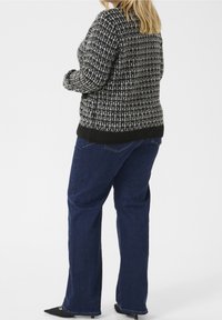 Schwarzer und weißer gemusterter Pullover mit strukturiertem Strick, kombiniert mit dunkelblauen geraden Jeans und schwarzen spitzen Absatzschuhen.