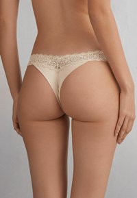 Naakt stringondergoed met een bloemenkant tailleband, voorzien van een soepele stoftextuur en minimale achterkant bedekking.