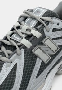 Gray running shoe with a textured mesh upper, white accents, curved design, and prominent logo detail on the side. Laces are light gray.