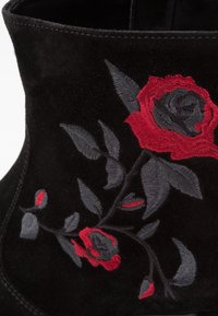 Czarne zamszowe botki za kostkę z czerwonym i szarym haftem róż oraz zielonymi liśćmi, gładka tekstura i zarysowany kształt.