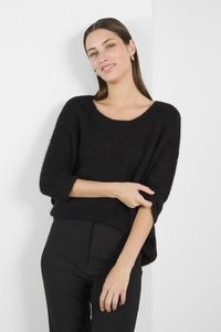 Melnā adīta džemperis ar brīvu piegriezumu, plašu kakla izgriezumu un trīs ceturtdaļu piedurknēm, kombinēts ar augsto vidukļa melno biksēm. Minimālisma dizains.