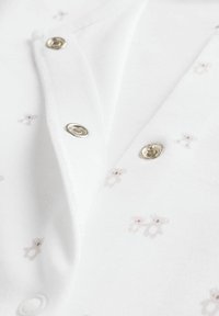 Cotton bodysuit with a white background, featuring a soft texture and small, light brown bear patterns. Snap fasteners visible at the collar.