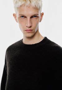 Crni pleteni džemper s okruglim vratnim izrezom, izrađen od mekog, teksturiranog materijala. Ima opušteni kroj i minimalistički dizajn.